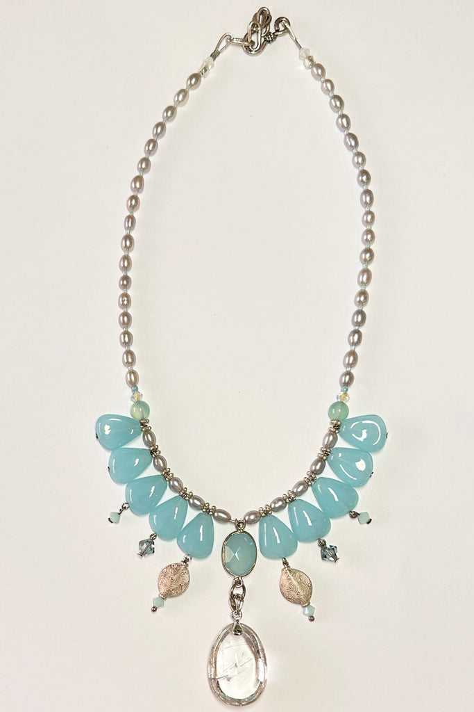 This pretty necklace is a one off piece made exclusively for Mombasa Rose Boutique, the hanging beads are aquamarine sea blue glass. The centrepiece is a gorgeous clear rutilated quartz. The necklace is of pale silvery grey natural pearls. This necklace is inspired by the ocean waves.