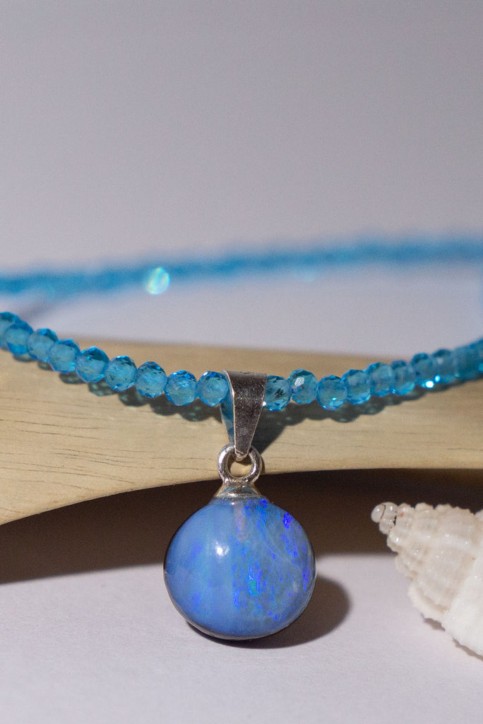 Blue as the sky on a summers day, this lovely opal is cut into a small round it hangs from a faceted blue Topaz gemstone bead necklace that sparkles in the light.