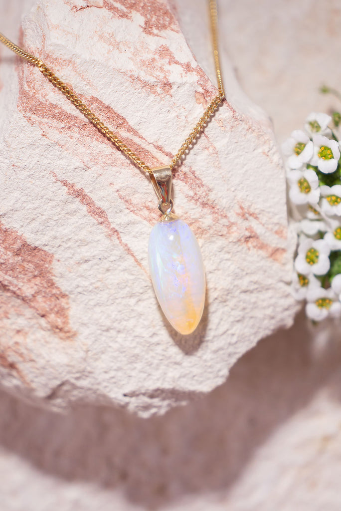 In perfect harmony, this magical crystal opal pendant is in a soft drop shape, it has blue and mauve in a pale pinky gold crystal, with a clear band running down the centre.