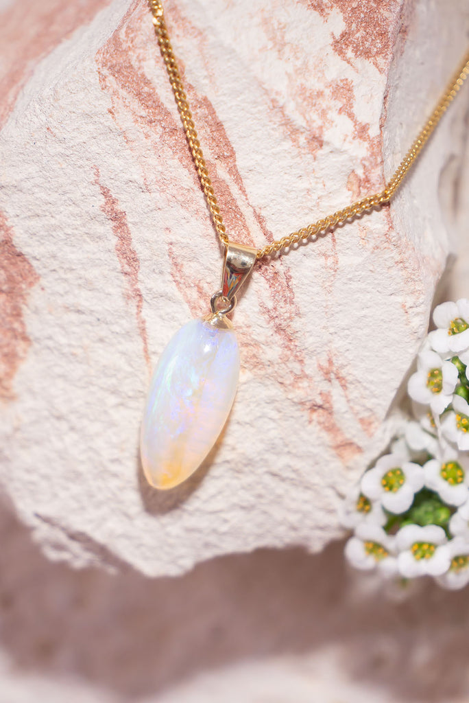 In perfect harmony, this magical crystal opal pendant is in a soft drop shape, it has blue and mauve in a pale pinky gold crystal, with a clear band running down the centre.